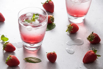 Glasses of strawberry water  with strawberries, ice and fresh mint leaves  on concrete background stone strong light with glass shadows. Copy space. Close up