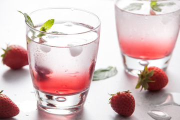 Glasses of strawberry water  with strawberries, ice and fresh mint leaves  on concrete background stone strong light with glass shadows. Copy space. Close up