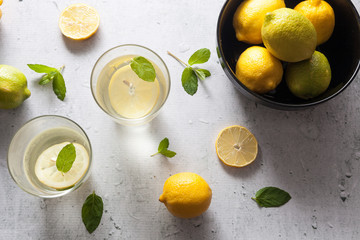 Glasses of water lamonade with lemon slices and fresh mint leaves green and yellow lemon on concrete background stone. Copy space. Flatlay, top view.