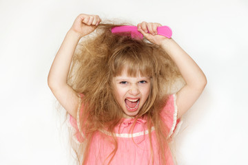 a little girl with unruly, tangled long hair in a pink dress on a white background tries to comb it