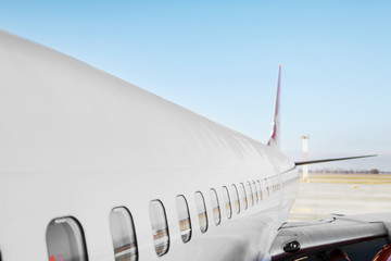 Aircraft porthole - side window airplain. White heavy passenger jet engine airplane on runway at airport against blue sky aviation transportation theme background.