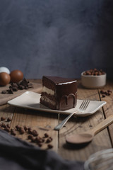 Chololate cake slice over a white plate on wooden table. Decorated with ingredients.