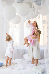 Young woman playing on the bed with the two daughters at home. Stay home and family concept.