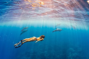 Fototapeten Frau im Bikini und Flossen, die an einem sonnigen Tag mit Delfinen im klaren blauen Meer schnorcheln © Melissa