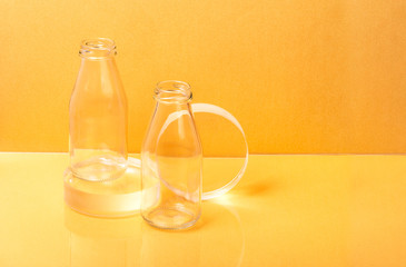 Glass bottles milk packaging on clear sphere shape stands on orange background. Creative minimalist still life