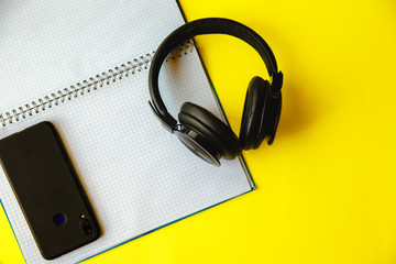 A large open notebook in a cage, headphones and a smartphone on a yellow background. Flat layout with space for text