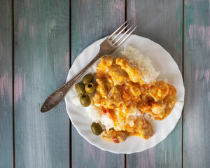 Breakfast of rice and stewed chicken fillet on a white plate on a wooden tray