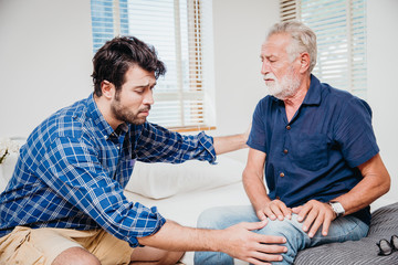 Young men health care elderly uncle in the home, old man pain at knee leg.