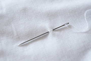 Needle and thread on white cloth close-up