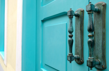 Elegant wooden door in blue green color with two old metal bronze ornamental handles.