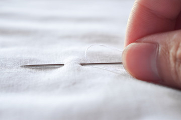 Fingers hands of the seamstress is using a needle and white thread to sew cloth close-up.