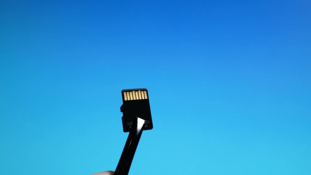 Micro SD memory card close-up on blue background sandwiched in crimper
