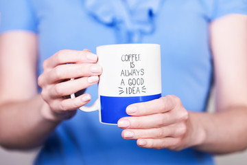 Female hands holding white blue cup with inscription " Coffee is always a good idea".  Break time concept 