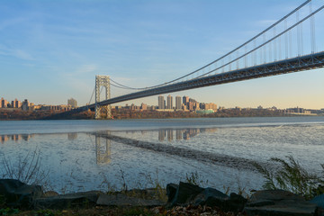 View of the George Washington Bridge from the NJ side with a view of Manhattan over the Hudson River with reflections on the water
