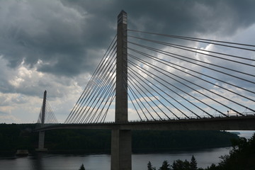 Moody view of cable bridge over dark water with ominous shades of gray sky in Maine