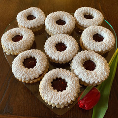 Close-up of Linzer cookies raspberry jam powdered sugar on top on a clear glass plate next to a red tulip