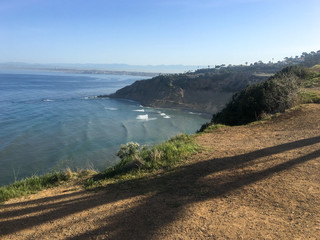 Pacific ocean view from cliff, distant cliffs and towns, strong shadows on brown dirt, green grass 