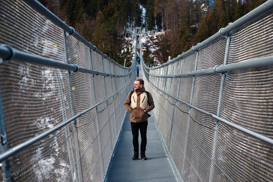 A young man in jacket stopped at the bridge during the hike, looking at the landscapes. Winter travel in Austria, Highline179