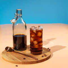 Cold brew coffee with ice cubes in glass on wooden tray,beige background,hard light