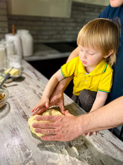 Obraz na płótnie Canvas A fair-skinned little child with his father / grandfather prepares sweet rolls filled with cottage cheese and raisins in the kitchen at home. A step-by-step cooking process.Defocus light background.