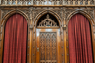 Ornate Gothic Wooden antique double confessional booth in Catholic church with red velvet curtains.