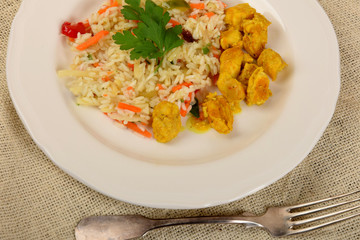 pieces of fried chicken in curry with rice and vegetables on a white plate