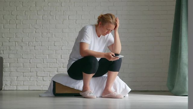 Upset stressed woman holding cellphone disgusted with message she received home background.