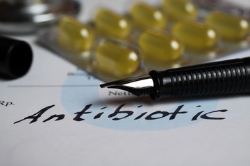 Fototapeta premium Macro closeup of isolated white prescription note, handwritten word antibiotic with pill blister and ink pen (Focus on tip of pencil)