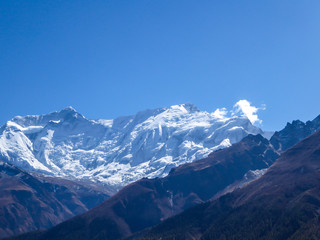 Fototapeta na wymiar A close up view on snow caped Himalayan peak seen from Annapurna Circuit Trek, Nepal. Sharp and steep slopes of the mountain. Powder snow being blown by strong wind. First sunbeams reaching the peak