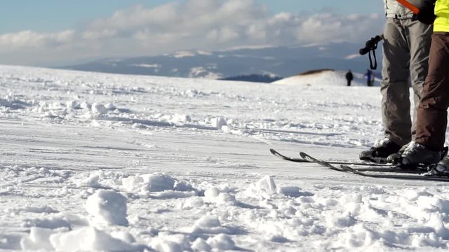 A skiers silhouettes in a ski boots slowly moving uphill leaving traces in the snow on a cloudy blue sky background, close-up. Ski resort in the snowy mountain woods on a bright winter day.