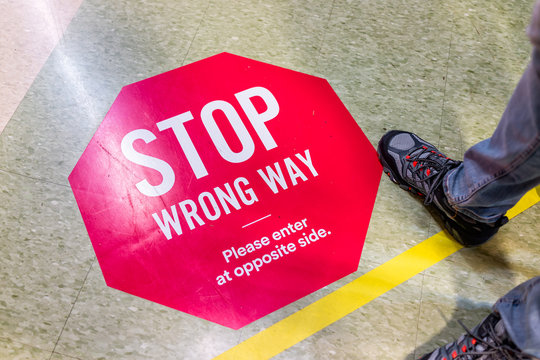 Red warning stop direction sign for entering wrong way in store aisle during covid-19 coronavirus outbreak with feet legs of person people in USA