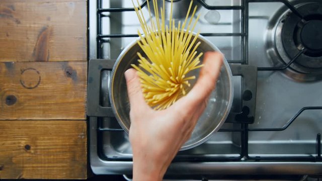 Top view on silver pot of boiling water on kitchen stove. Female chef adds authentic italian spaghetti pasta in symmetric and professional way. Cooking at home, food or cook blog
