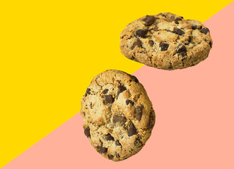 Two homemade chocolate chips cookies flying in air on diagonal duotone pink yellow background. Baking kids birthday party sweets concept. Banner poster for cafes coffee shops with copy space