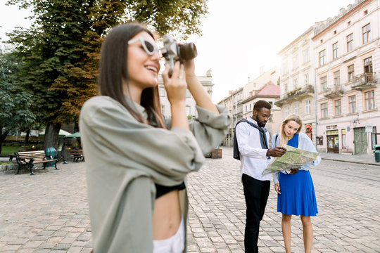 Young beautiful tourist woman exploring the city, making photos of famous places. African man and Caucasian girl holding city map and exploring new city vibes. Travel, friendship concept