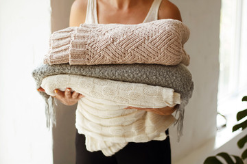 Close up picture of woman’s hands holding many different warm clothes and blankets