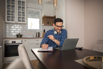Businessman writing notes in his notebook while using laptop.