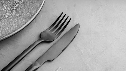 A black Matt fork and knife lie next to a gray plate with the texture of concrete.