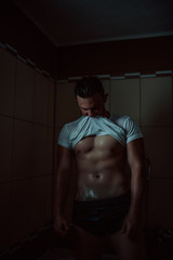Fototapeta na wymiar Sexy young muscle man in a shower wearing dark underwear and wet white t-shirt