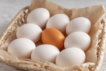 One orange egg among white in one wicker basket.