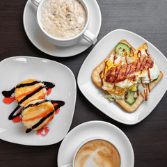 Breakfast consists of oatmeal porridge with cheesecakes and cappuccino with sandwich, top view.
