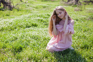 Beautiful blonde woman in pink dress collects flowers in flowering garden