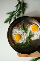 Two fried eggs in pan sprinkled with ground black pepper on white buckround.
