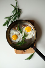 Two fried eggs in cast iron frying pan sprinkled with ground black pepper on white buckround.