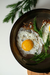 Two fried eggs in pan sprinkled with ground black pepper on white buckroun closeup. 