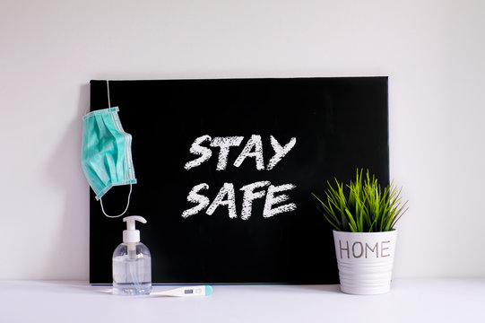 Stay Safe Stay Home message concept on a black chalkboard with cirurgical face mask for covid-19, hand gel and a plant on a desk, isolation during quarantine