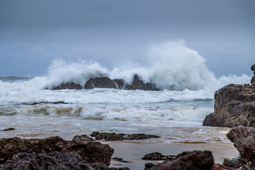 Rocks next to the beach of the Camel Rock bay in New South Wales, Australia at a cloudy and windy day in summer with strong waves in the ocean. 