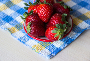 Strawberry background. A plate of fresh strawberries sits on a checkered tablecloth on a wooden table, copy space. Sweet, ripe strawberries. Harvest of organic local  strawberries. Healthy food.