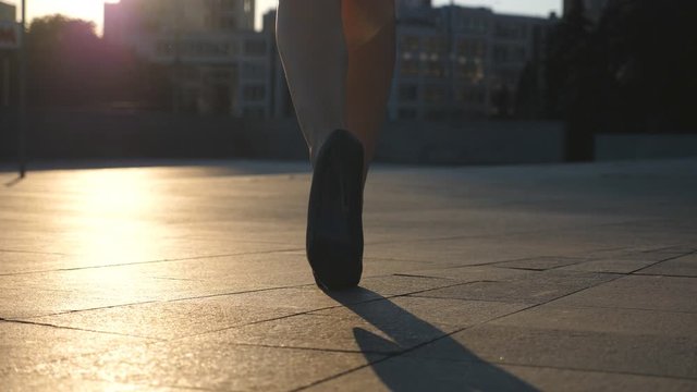 Female legs in high heels shoes walking in the urban street with sun flare at background. Feet of young business woman in high-heeled footwear going in the city. Girl stepping to work. Slow motion