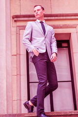 Young Businessman Street Fashion in New York City. European Man wearing gray blazer, white shirt, black tie, black pants, leather shoes, walking down stairs outside office. Color filtered effect..