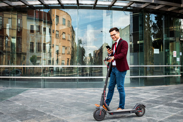 Smiling businessman with electric scooter standing in front of modern business building looking at...